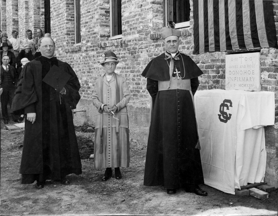Catherine Donohoe with then-SCU President Zacheus Maher, S.J., and Archbishop of San Francisco Edward Hanna at the unveiling of the Donohoe cornerstone in 1925. A woman and two men in dark robes (one in clerical robes and one in University regalia) at the unveiling of the Donohoe Infirmary building cornerstone in 1925.
