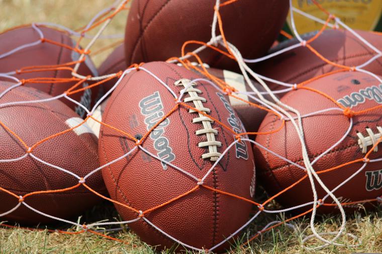 Several Wilson-branded footballs in a white and orange rope net. 