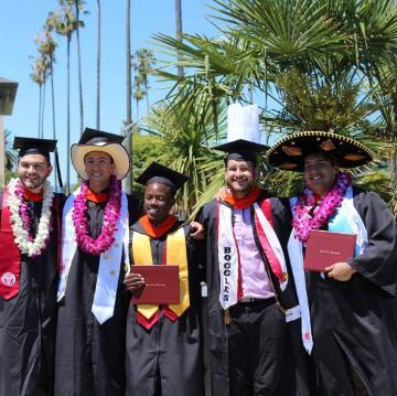 A group of graduates holding diplomas and wearing leis at commencement.