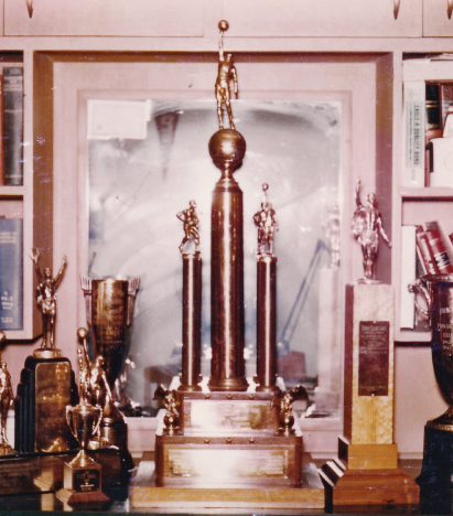 A vintage photo from 1957 of several USF sports trophies on a bookshelf