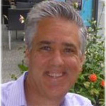 A smiling person outdoors, with greenery in the background.