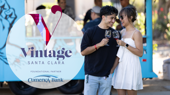 A young couple in front of a food truck stand close together, holding wine glasses in a 