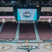 A basketball court with the WCC logo on the floor and on a TV screen coming down from the ceiling