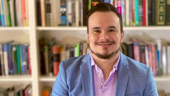 A smiling man in business wear, standing in front of a bookshelf.