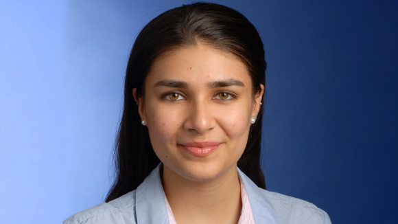A smiling young woman in business wear, in front of a blue background.