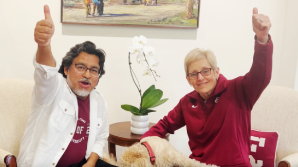 A man and a woman in Santa Clara University gear smile and make a thumbs up motion. 
