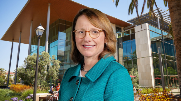 A smiling woman in glasses and a teal blazer in front of the SCU SCDI Building.
