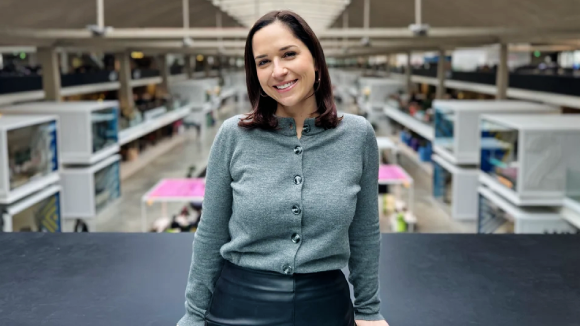 A smiling, dark-haired woman in front of a factory floor.