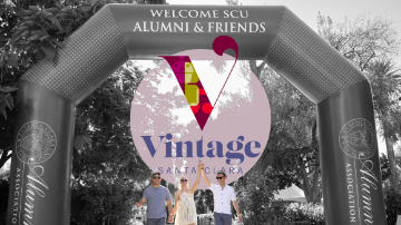 Two men and a woman holding hands underneath an inflatable arch reading 