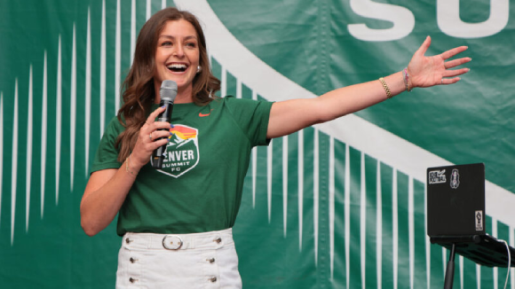A happy woman holding a microphone and wearing a green shirt with the 