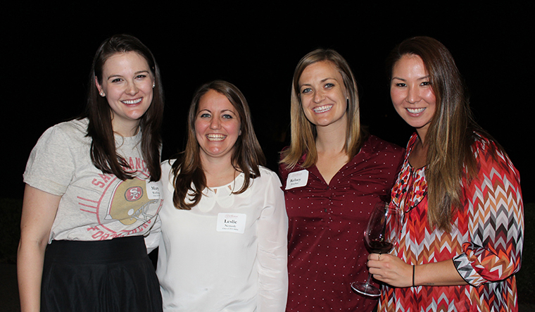Four individuals smiling and posing together against a black background.
