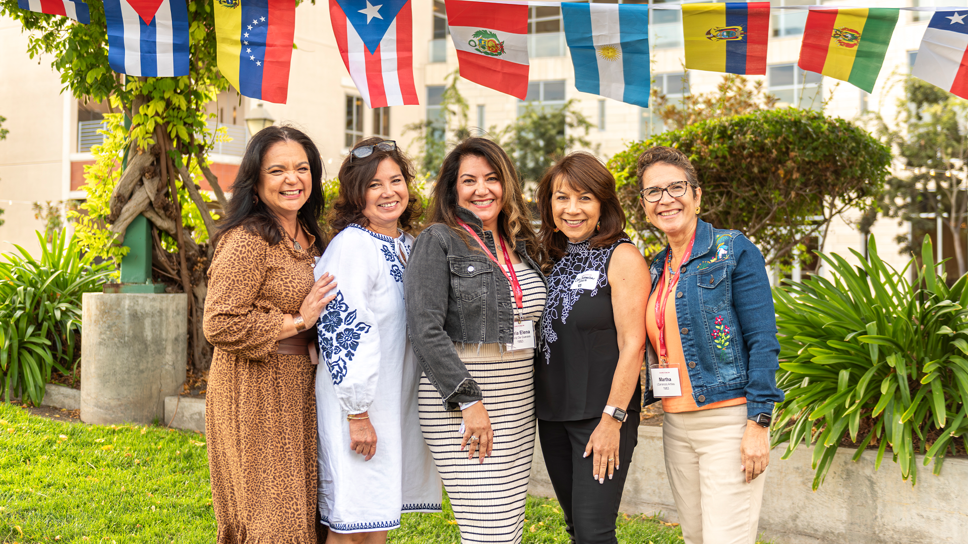 Five alumnae group together under flags that represent the Latinx community