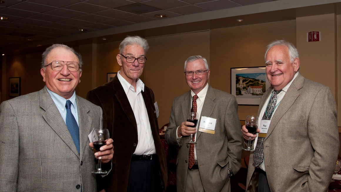 Four men holding wine glasses and smiling at the camera 