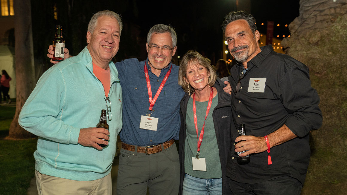 Four people standing arm-in-arm and smiling at the camera 