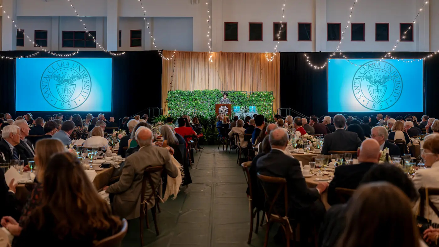 A large group of people in an elegant room looking at a speaker on a stage