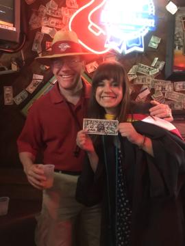 Two people smiling at a crowded event, one holding a sign reading 