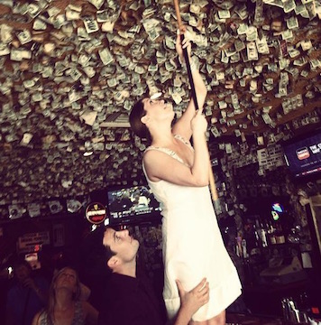 Person in white dress reaching up in a room with a decorative ceiling.