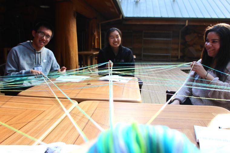 Three people sitting at a wooden table having a discussion.