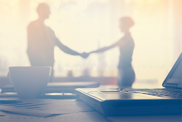 Two people shaking hands in a blurred office background.