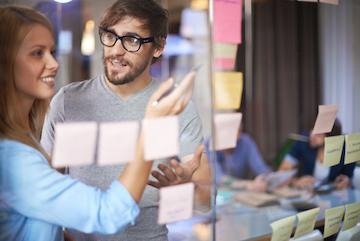 People collaborating in an office with sticky notes on a glass board.