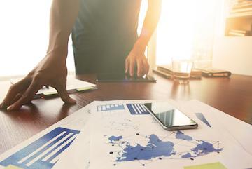 Person reviewing charts and documents on a desk with a pen and glasses.