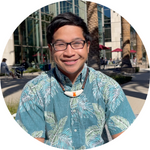 Smiling person in glasses outside near buildings on a sunny day.