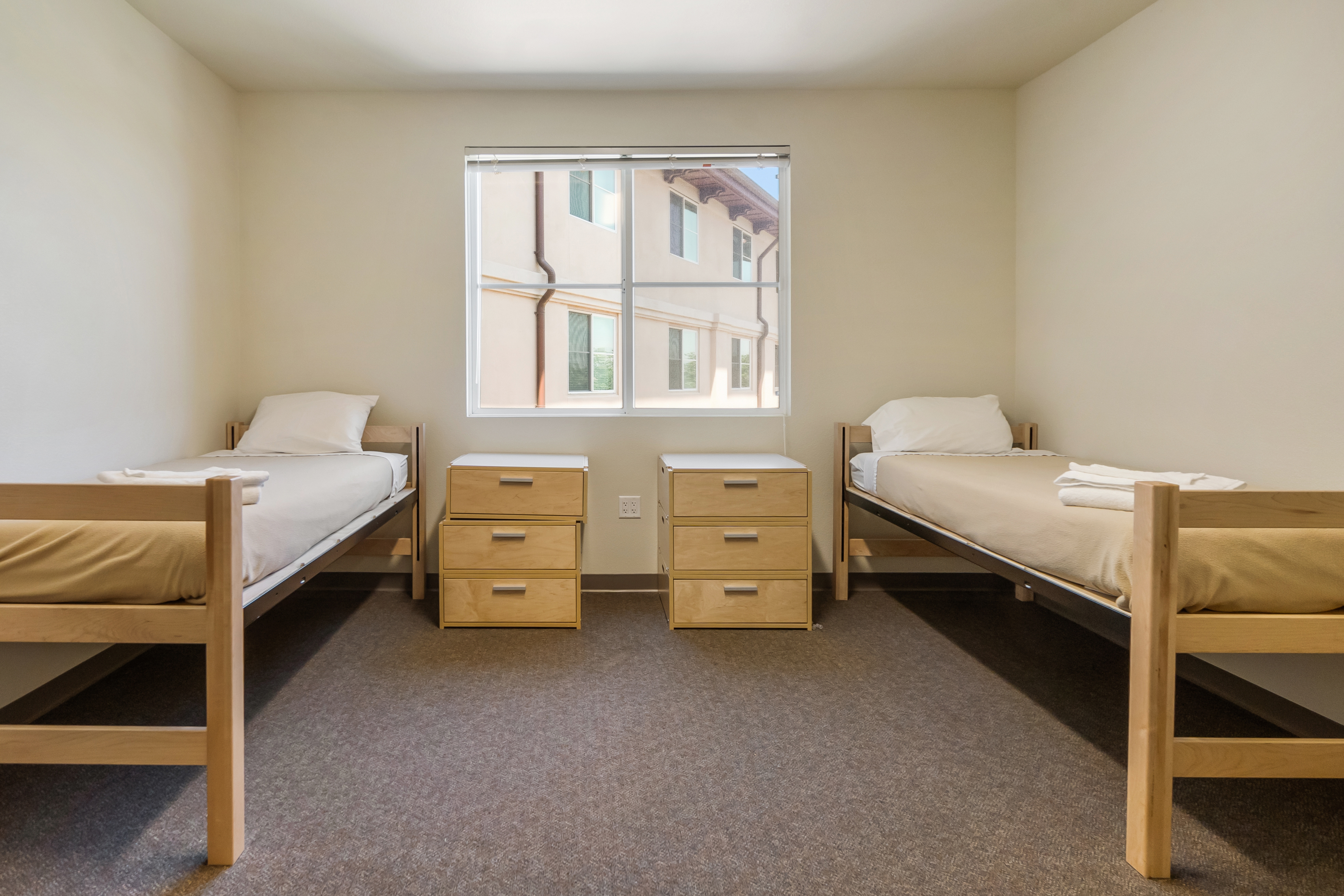 A tidy dorm room with two beds, desks, and a window.