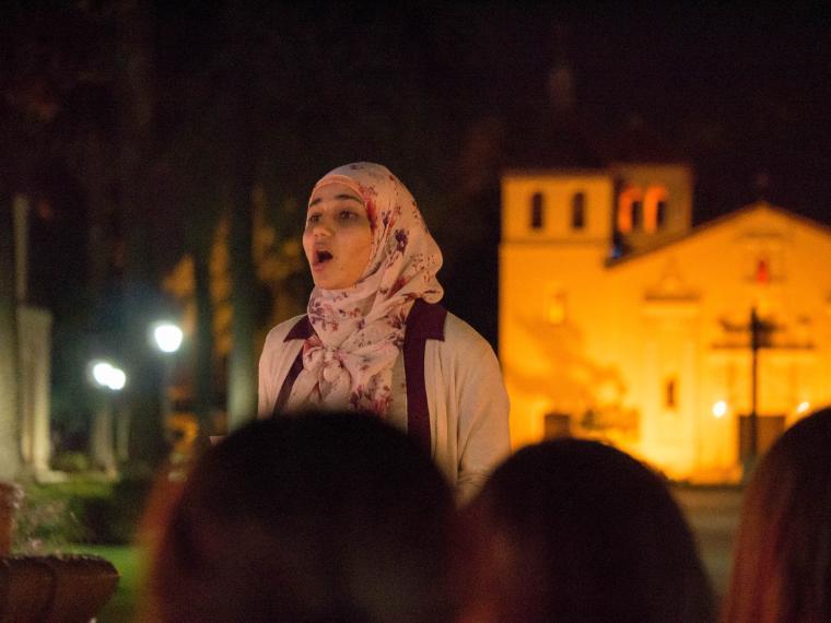 A speaker at a nighttime vigil with a lit building in the background.