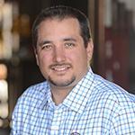 A man in a checked shirt, smiling at the camera.