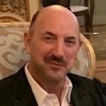 A man wearing a suit, seated and smiling.