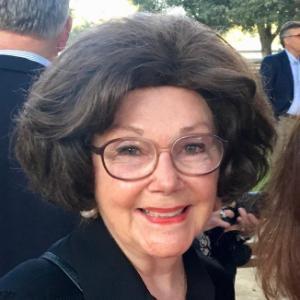 A smiling woman with glasses in an outdoor setting.