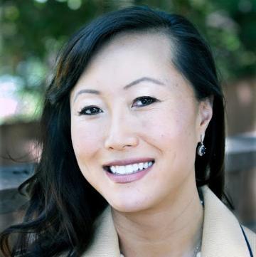 A person smiling outdoors, with a blurred background.