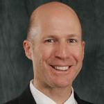 A man wearing a suit and tie smiles for a professional photo.
