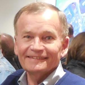 A smiling person in a blue shirt and sweater.