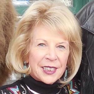 A woman smiling outdoors with light-colored hair.