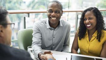 Couple smiles and shakes hands with someone across the table 