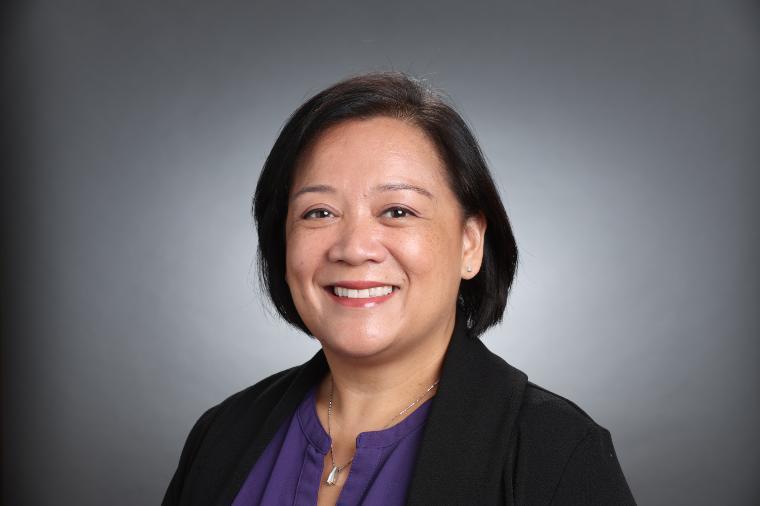 A person smiling in front of a gray background.