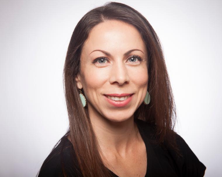 A woman smiling against a plain background.