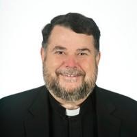 Man in clerical attire smiling with a white background. image link to story