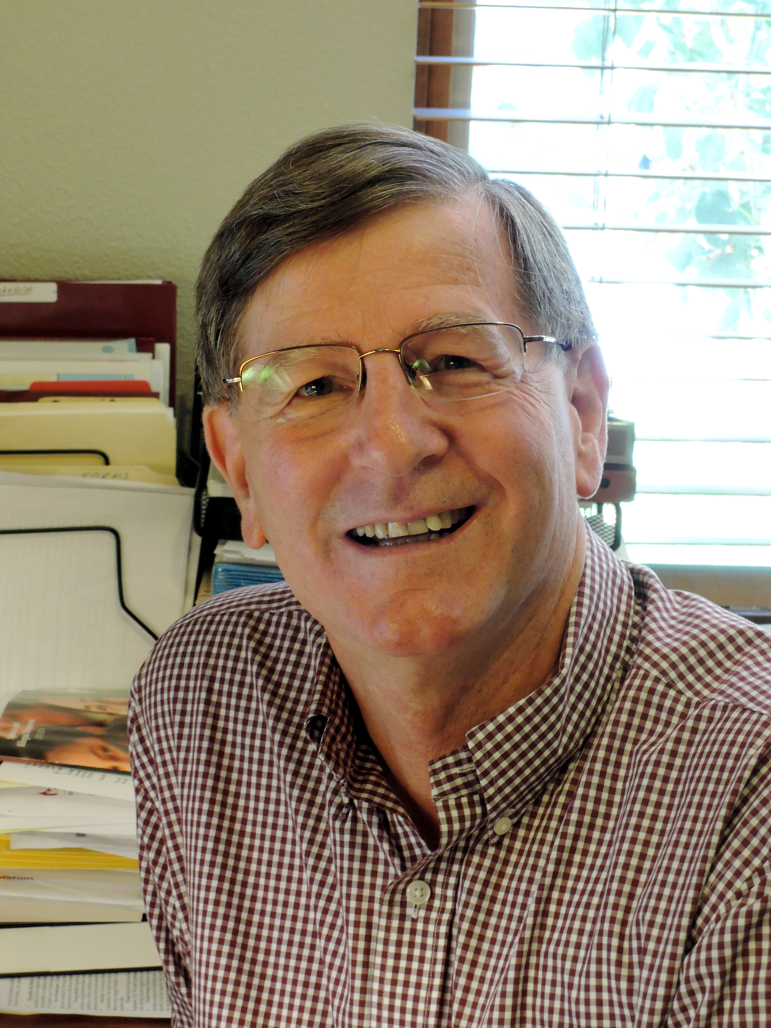 A person smiling in an office setting with books and papers nearby. image link to story
