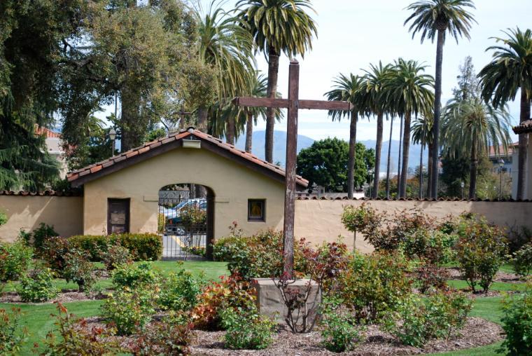 Small building in Rose Garden Cemetery surrounded by plants and palm trees.