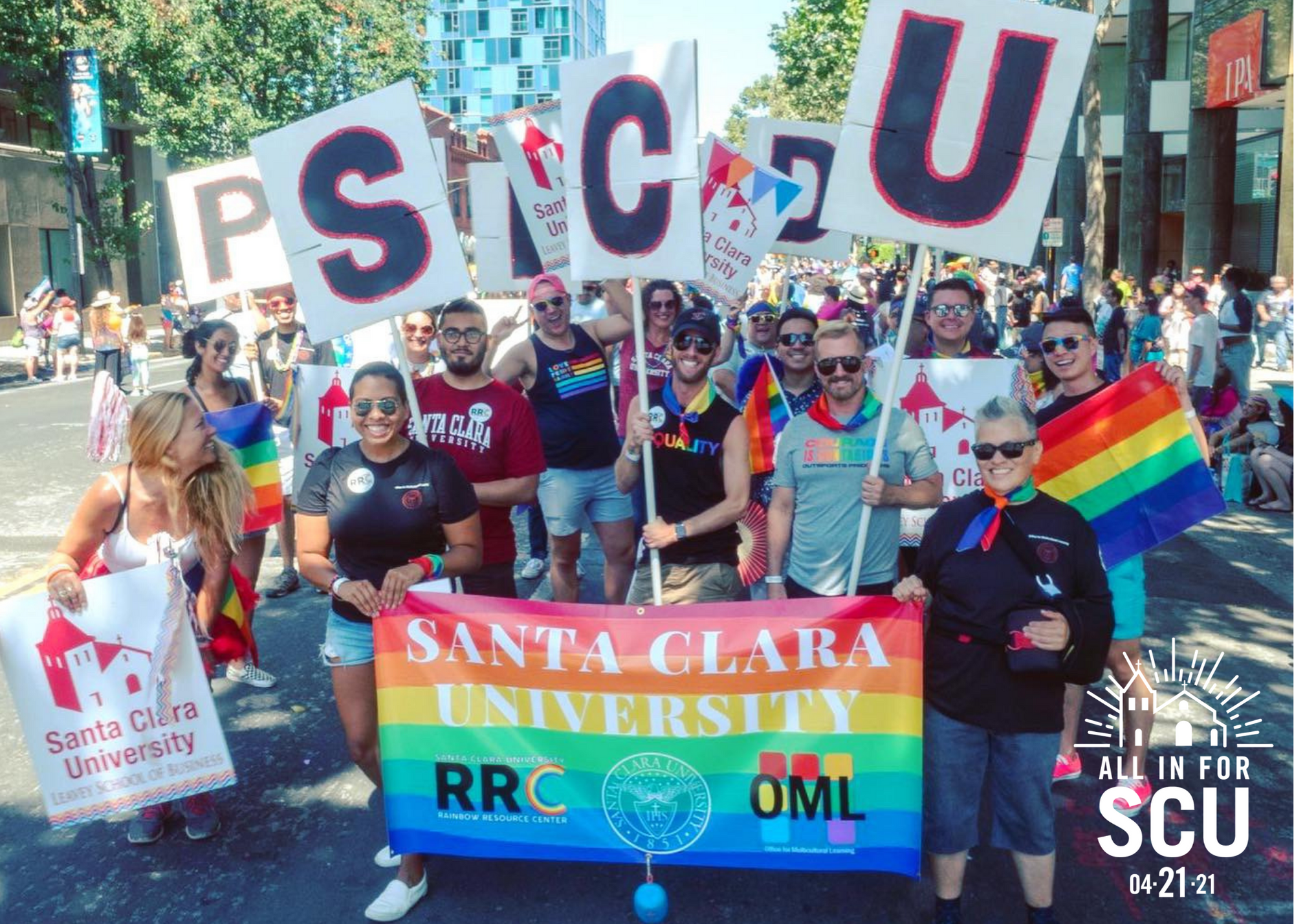 A group of people holding signs and a rainbow banner reading 