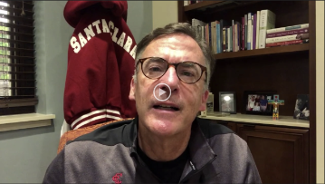 Man speaking in an office with bookshelves and a jacket in the background.
