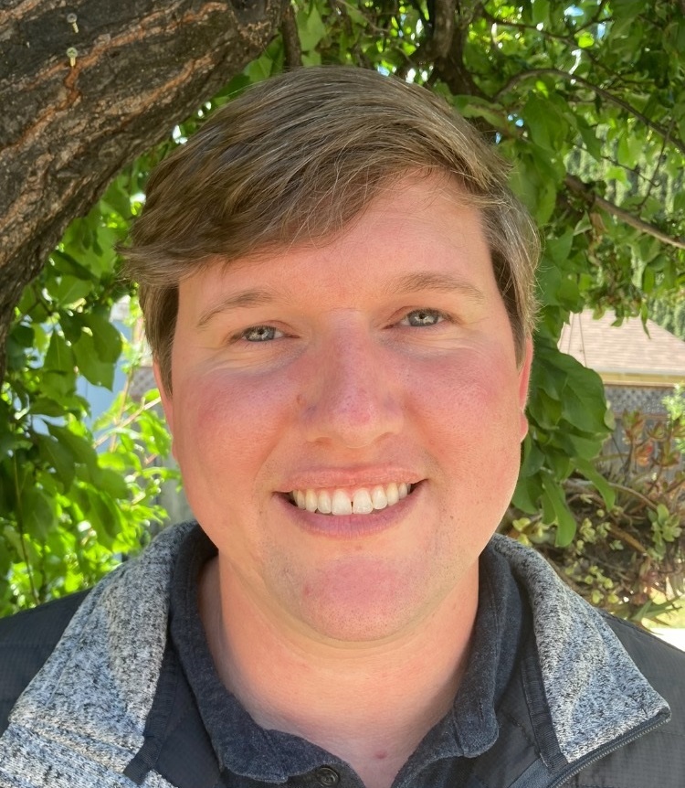 A person smiling in front of green foliage background.