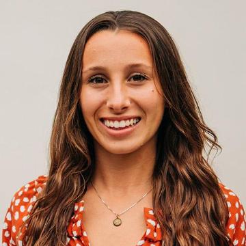 A woman smiling in a red patterned top.