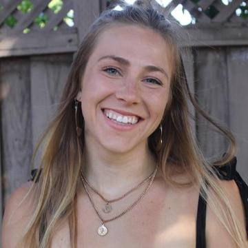 A person smiling in front of a wooden fence.