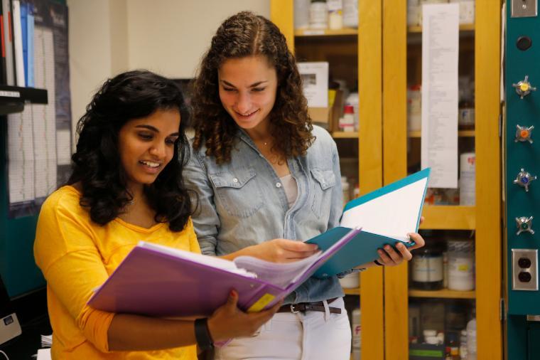 Two students looking at a book together in a classroom. image link to story