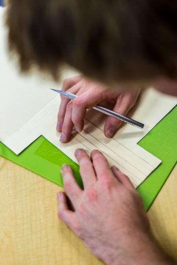 Student measuring and drawing lines on paper with a pencil and ruler.