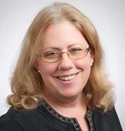 A person smiling with glasses, wearing a dark top. image link to story