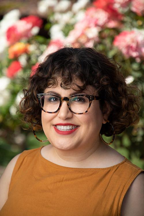 A person smiling in front of a background of colorful flowers. image link to story